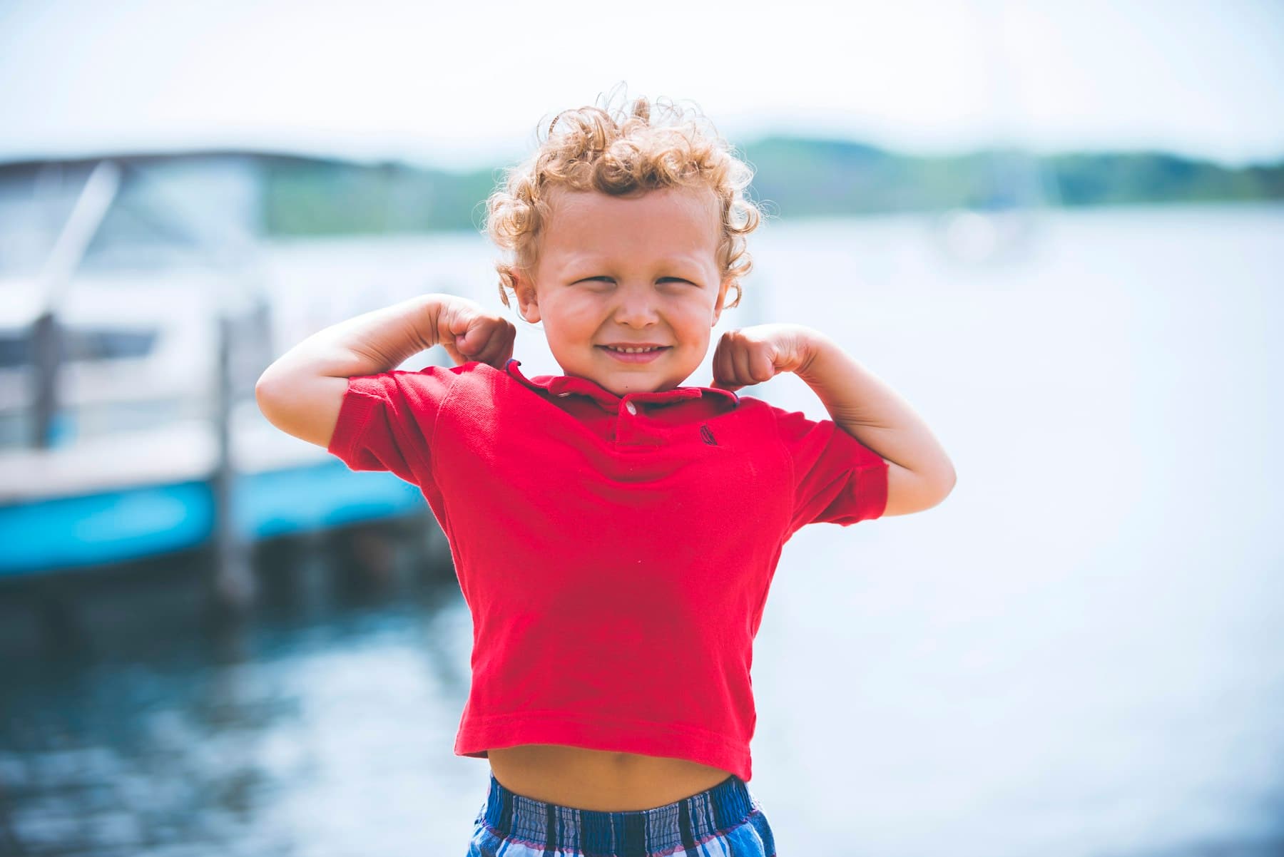 A young child smiling confidently outdoors by a lake